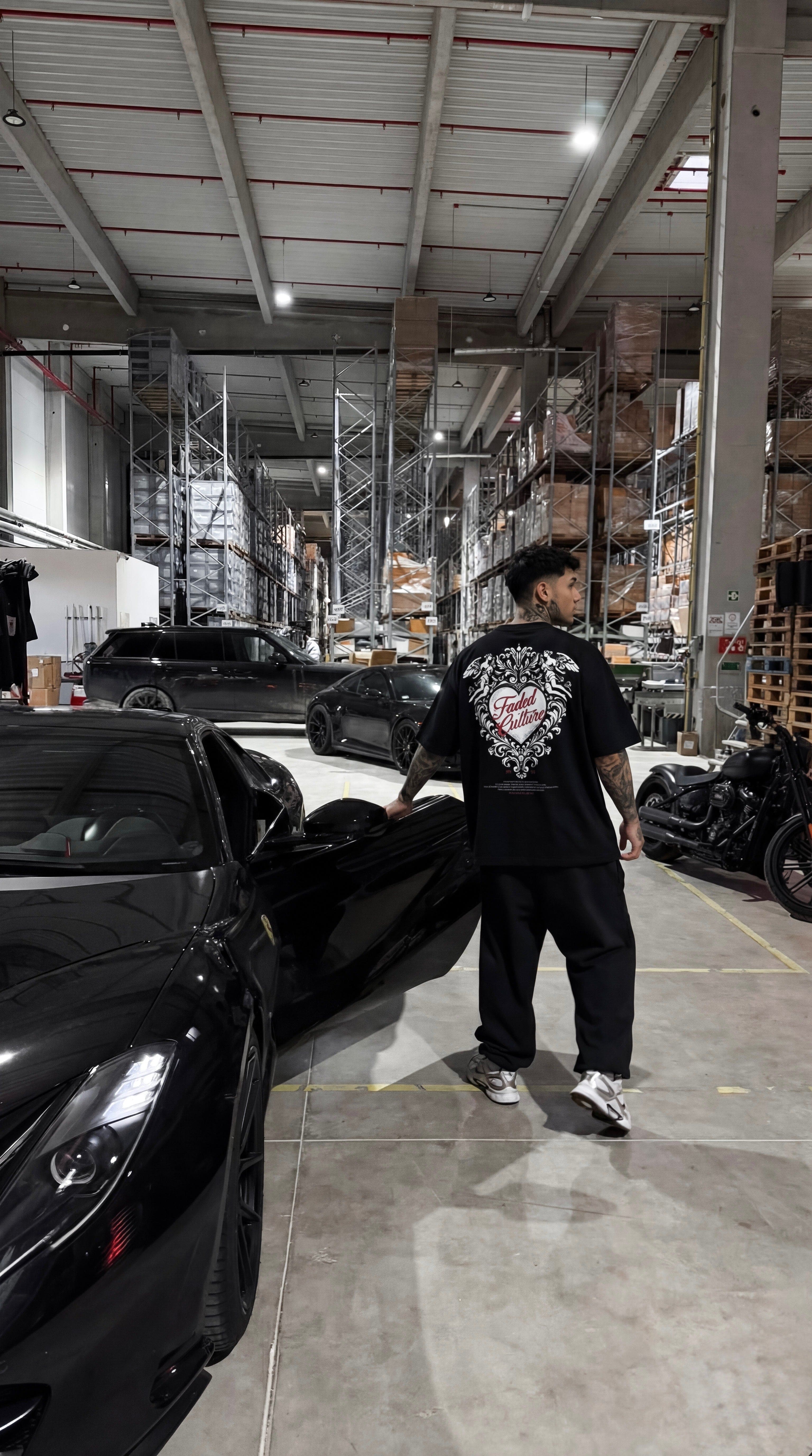 Person standing next to a black car in a warehouse setting